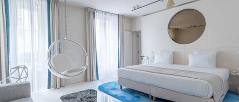A modern bedroom with a large bed, a hanging chair, and a round mirror on the wall.