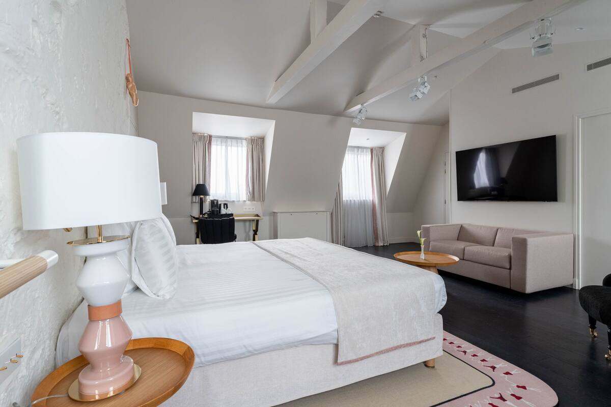 Una habitación de hotel moderna con una cama grande, un sofá, un televisor y un escritorio con lámpara.