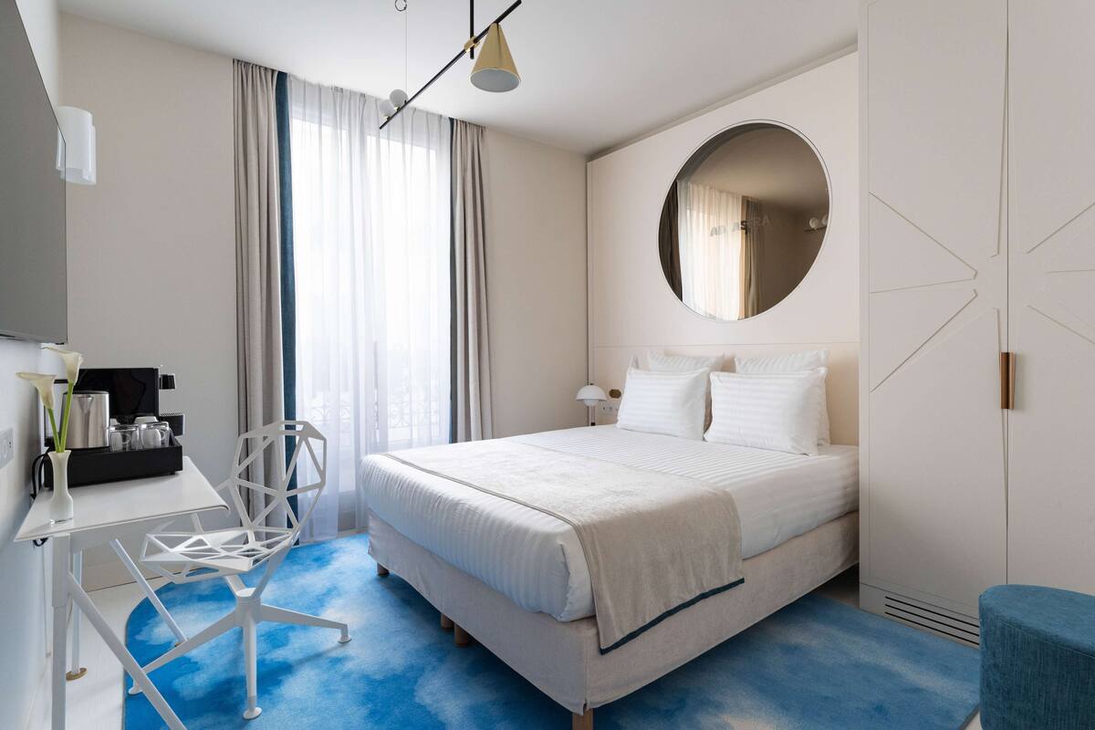 Una habitación de hotel moderna con una cama, un escritorio, una silla, un espejo redondo y un armario.