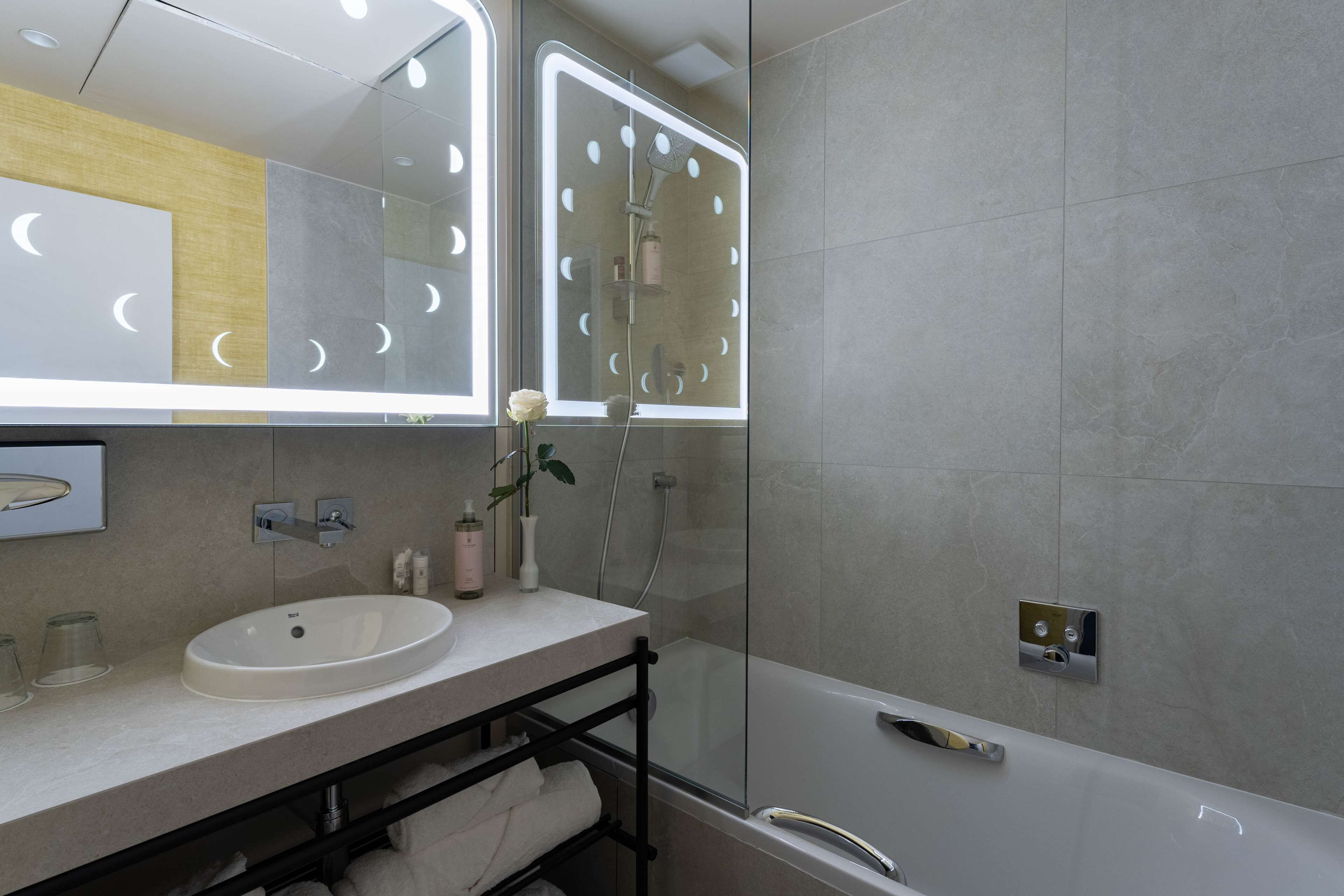 A modern bathroom with a large mirror, a sink, and a shower.