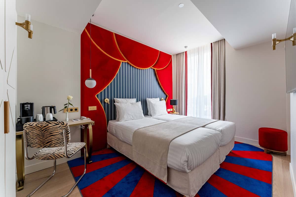 Una habitación de hotel moderna con una cama grande, un sillón estampado con motivos de cebra, una pared de acento roja y una alfombra a rayas.
