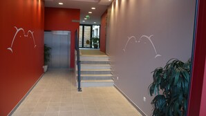 Un hall d’hôtel moderne avec un mur rouge, un escalier et un comptoir d’accueil.