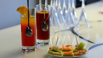 Dos bebidas con cucharas y un adorno de naranja, y un plato de aperitivos sobre una mesa.