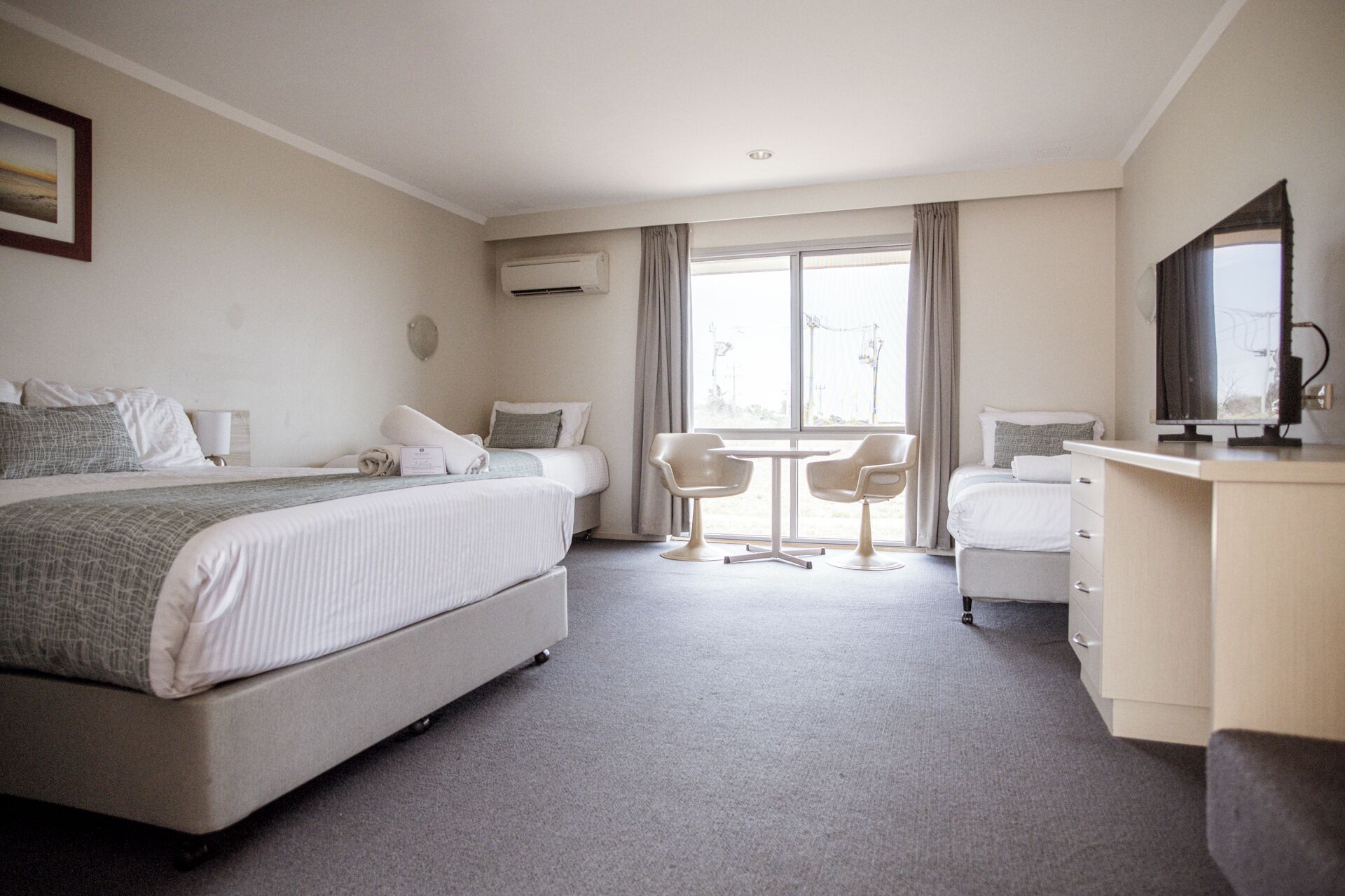 A hotel room with two beds, a desk, a chair, and a television.