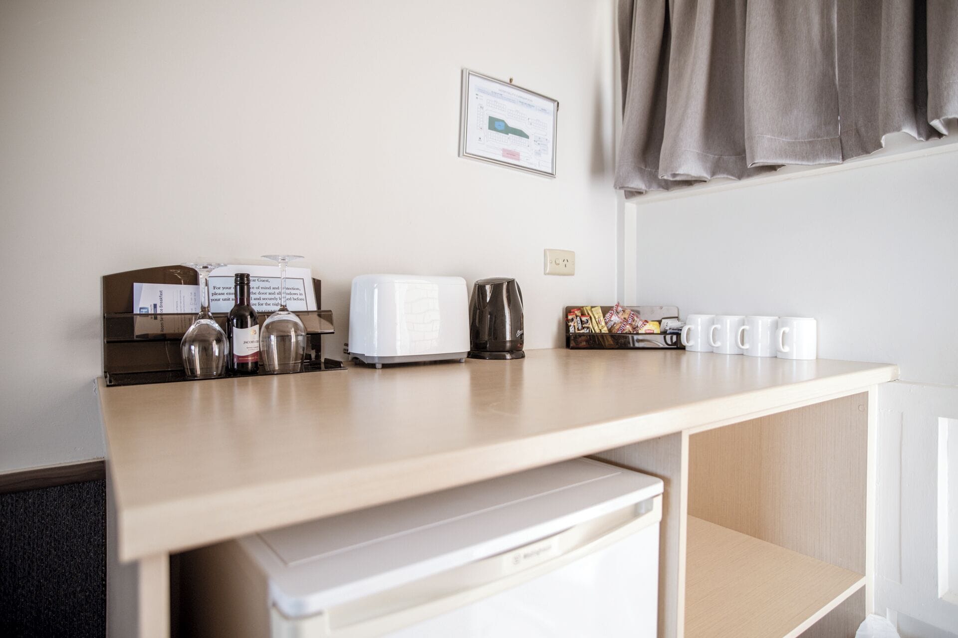 A kitchenette with a toaster, kettle, and coffee maker. There are white mugs and a snack bar on the counter.