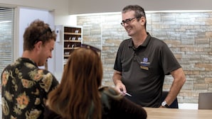 A reception area with a stone wall, a flat-screen TV mounted above a reception desk, and a person in a black shirt with a name tag. - Hospitality Carnarvon, SureStay Collection by Best Western (South Carnarvon)