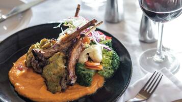 A plate of food with a lamb shank, vegetables, and a sauce, accompanied by a glass of red wine.
