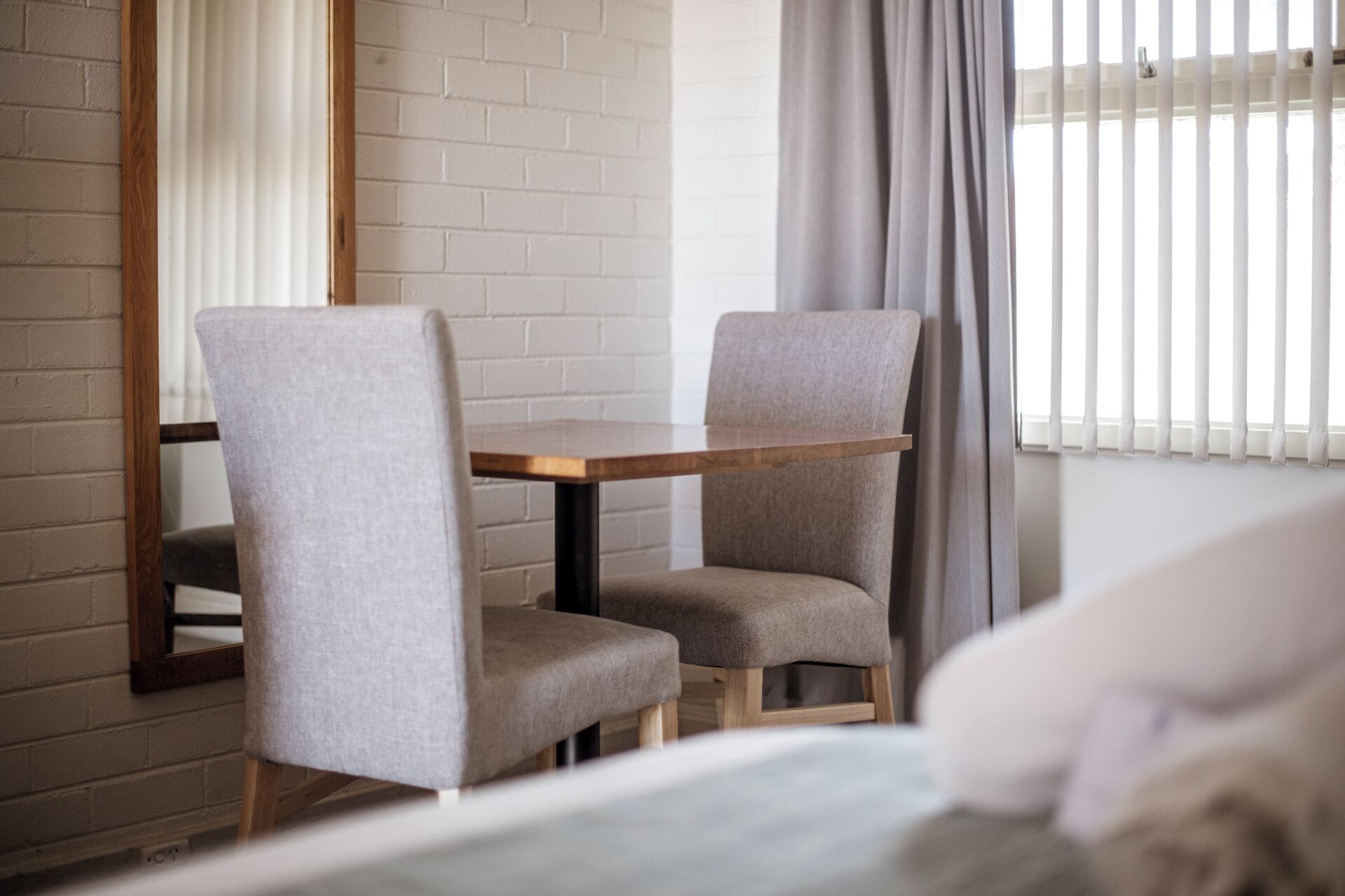 Una habitación con dos sillones grises tapizados, una mesa de madera y una ventana con persianas verticales.
