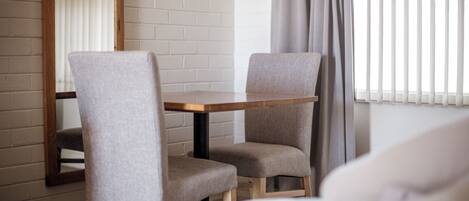 Una habitación con dos sillones grises tapizados, una mesa de madera y una ventana con persianas verticales.