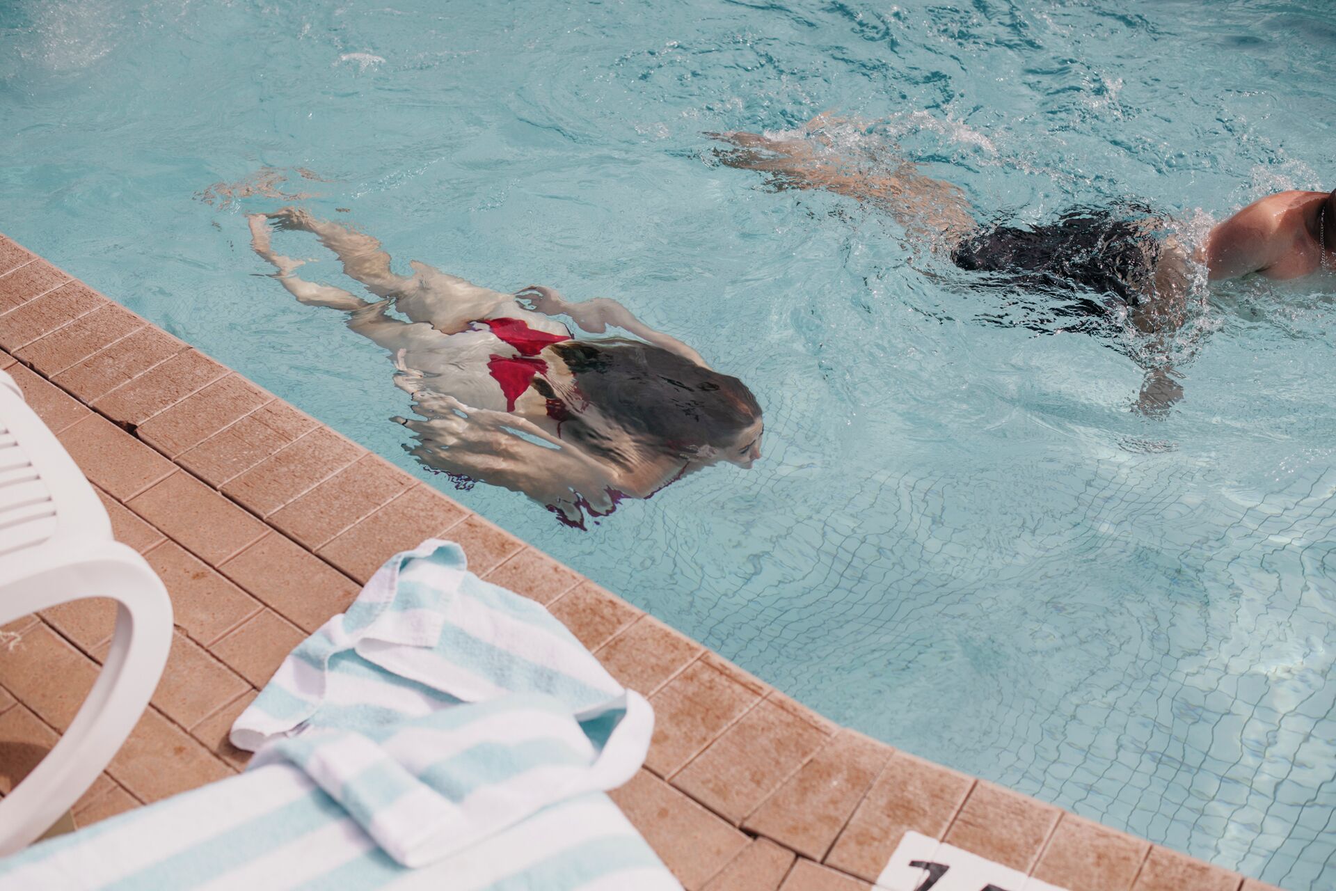 Una piscina con borde de azulejos y una toalla al lado.