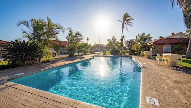 A rectangular swimming pool with clear blue water, surrounded by a paved walkway and palm trees. - Hospitality Carnarvon, SureStay Collection by Best Western (South Carnarvon)