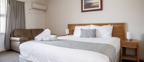 Una habitación de hotel con una cama grande, un sofá, una mesita de noche y un cuadro en la pared.