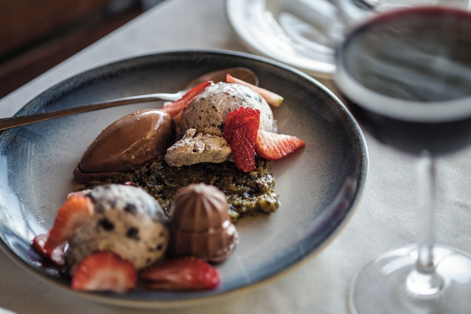 Un plato de postre con diferentes sabores de helado y fresas sobre una fuente de cerámica.