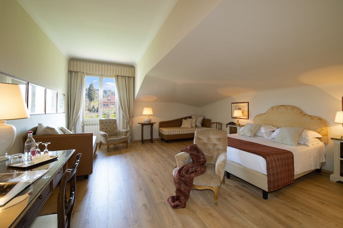 A hotel room with a bed, a sofa, a desk with a lamp, a chair, and a view of the outside.