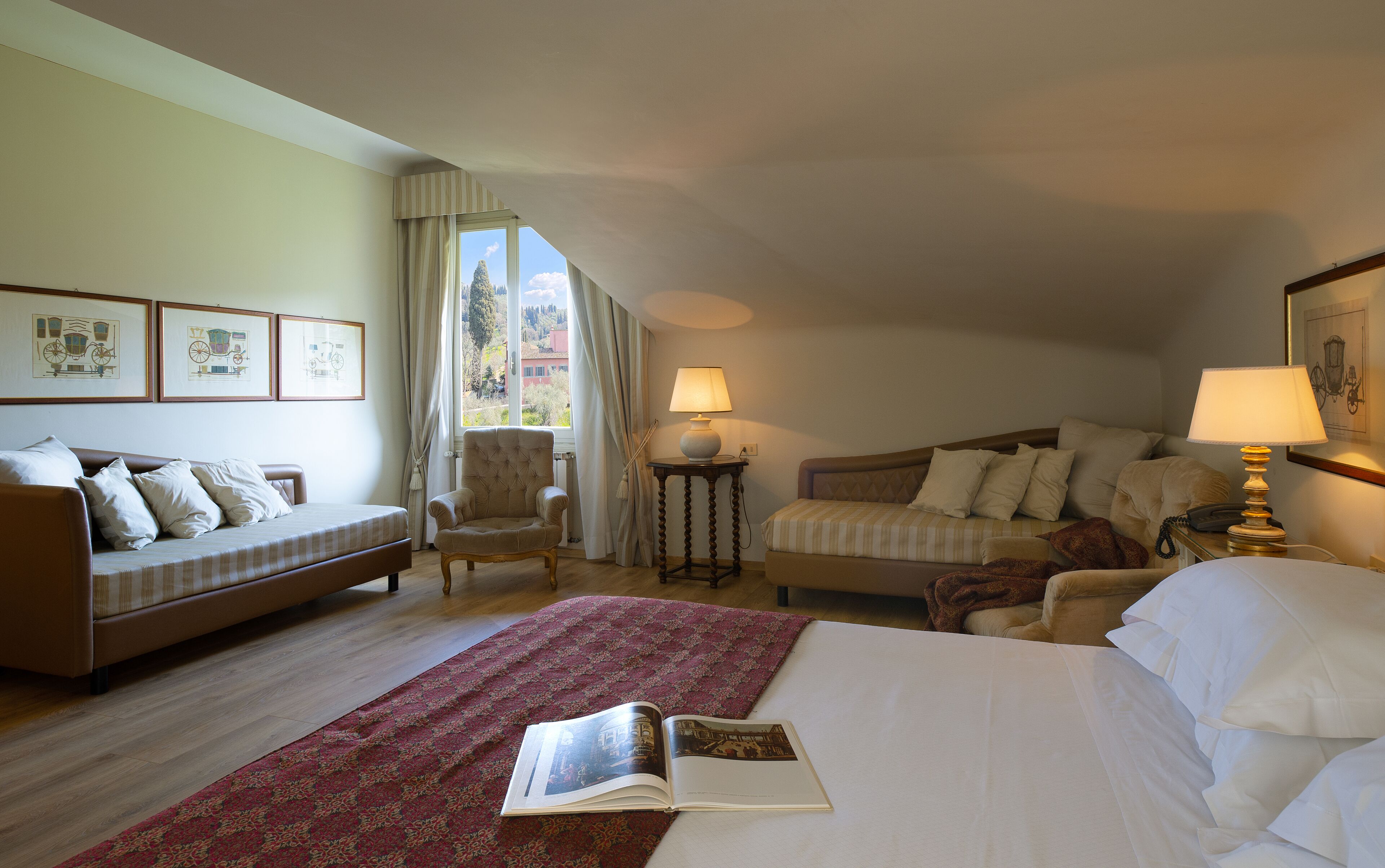 A bedroom with a bed, two sofas, a chair, a table with lamps, and a window with curtains.