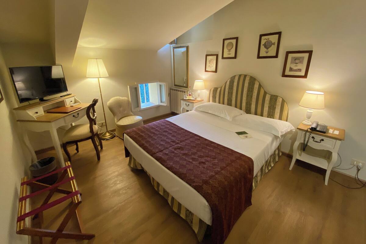 A hotel room with a bed, desk, chair, TV, and bedside lamps.