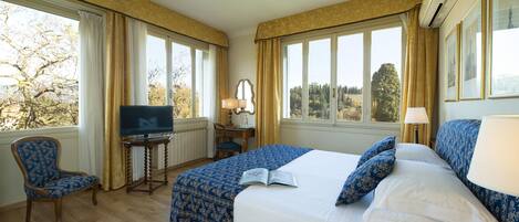 A hotel room with a large bed, a desk with a chair, a television, and large windows with curtains.