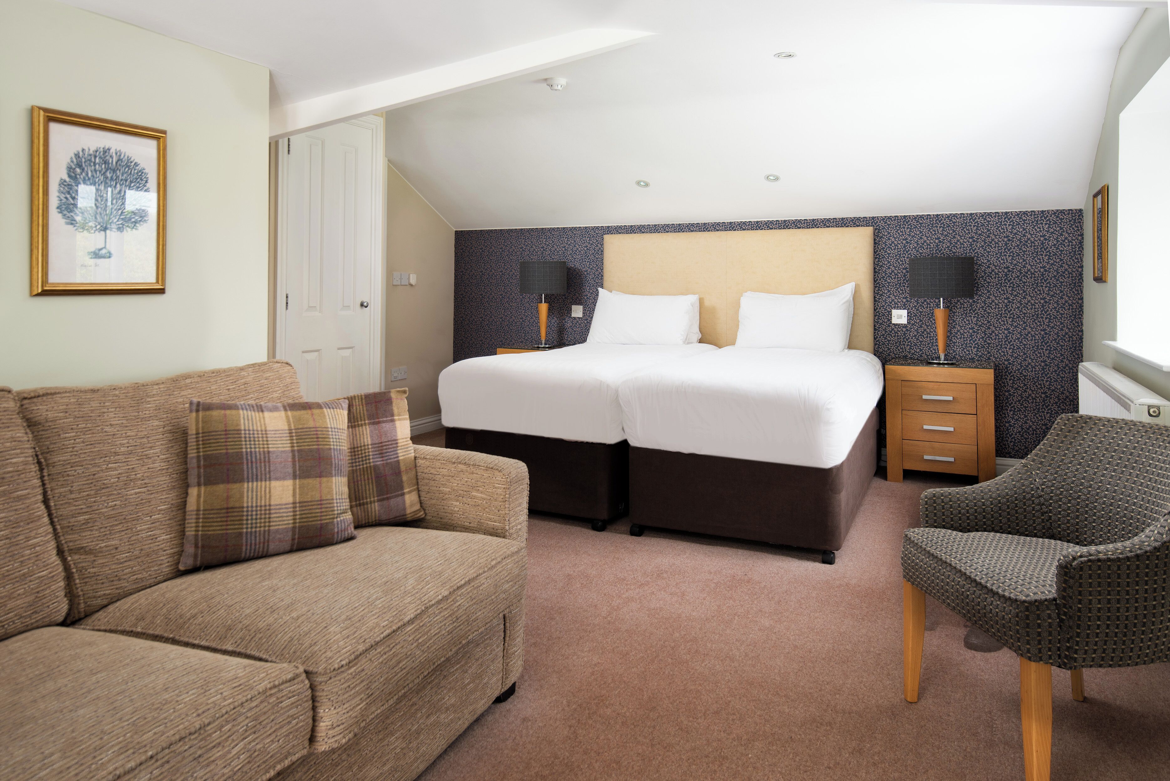 A hotel room with a double bed, a sofa, a chair, and a nightstand with lamps.