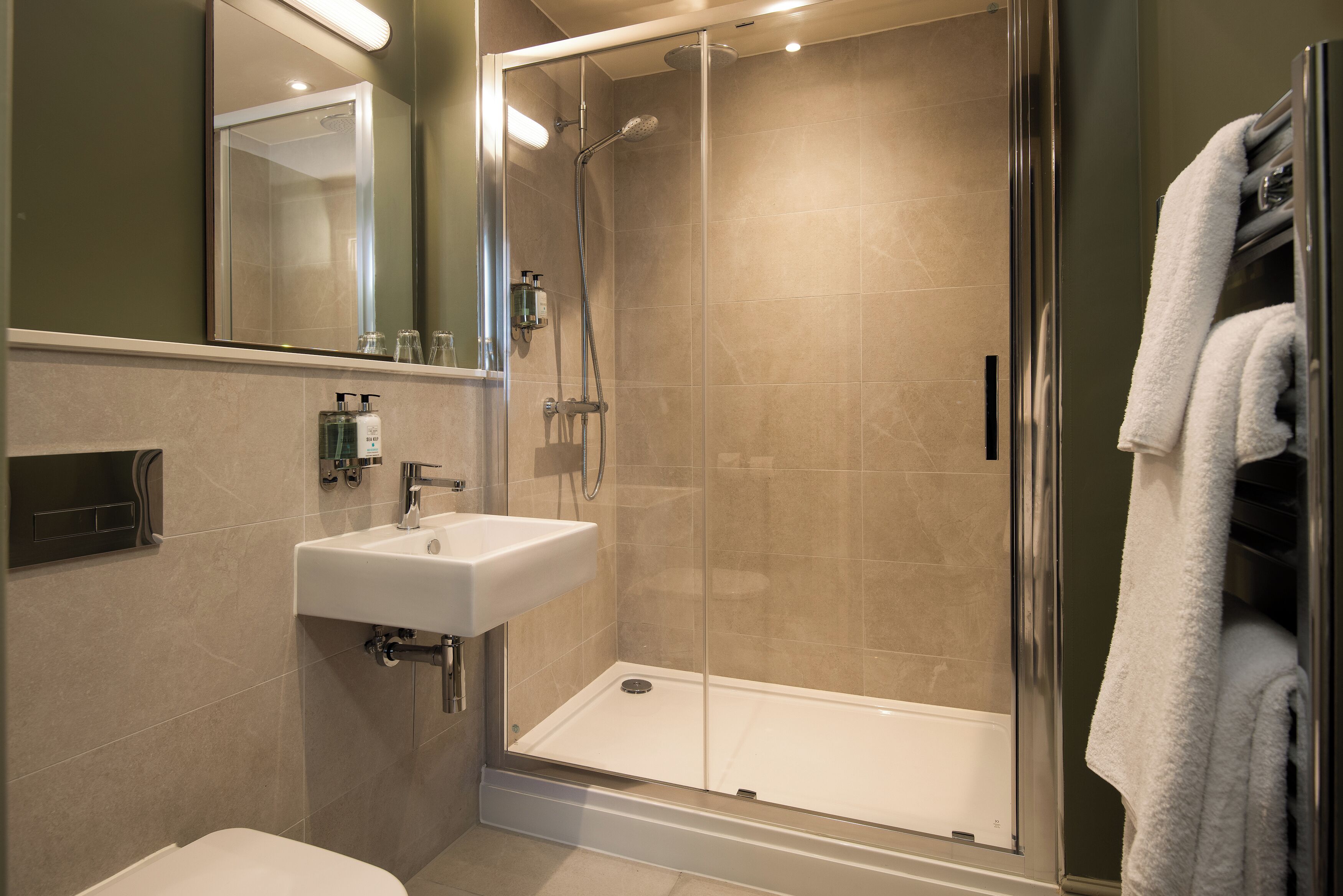 Un baño moderno con ducha de vidrio, lavamanos blanco y perchero para toallas.