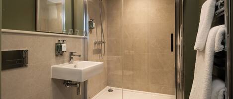 Un baño moderno con ducha de vidrio, lavamanos blanco y perchero para toallas.