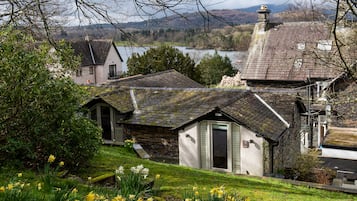 A stone house with a sloped roof, a small attached shed, and a garden with daffodils.