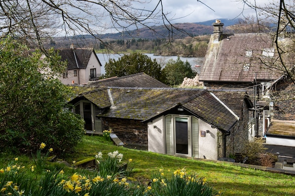A stone house with a sloped roof, a small attached shed, and a garden with daffodils. - Lakehouse at The Waterhead Inn (Ambleside)