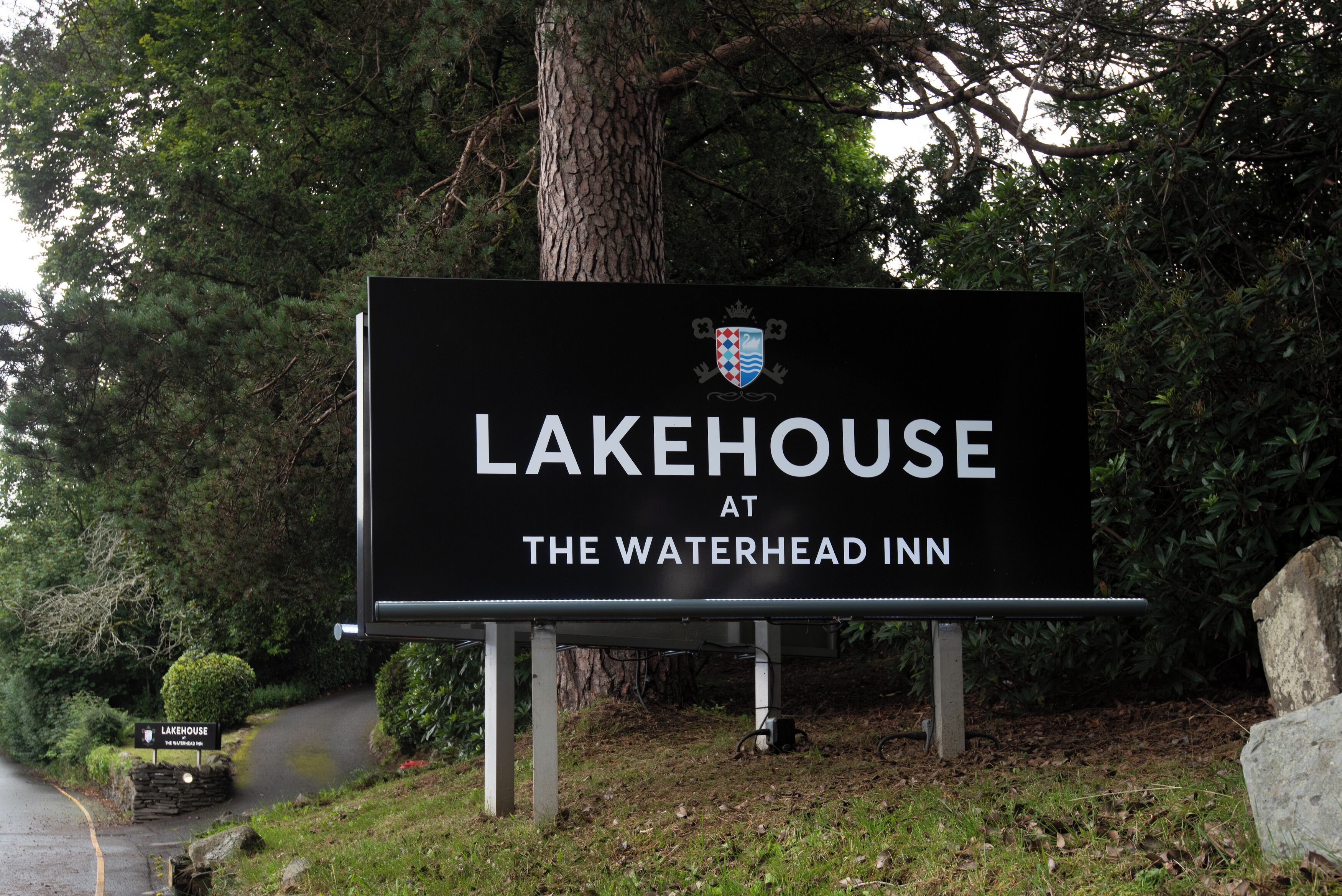 A sign for Lakehouse at The Waterhead Inn, surrounded by trees and a stone wall.