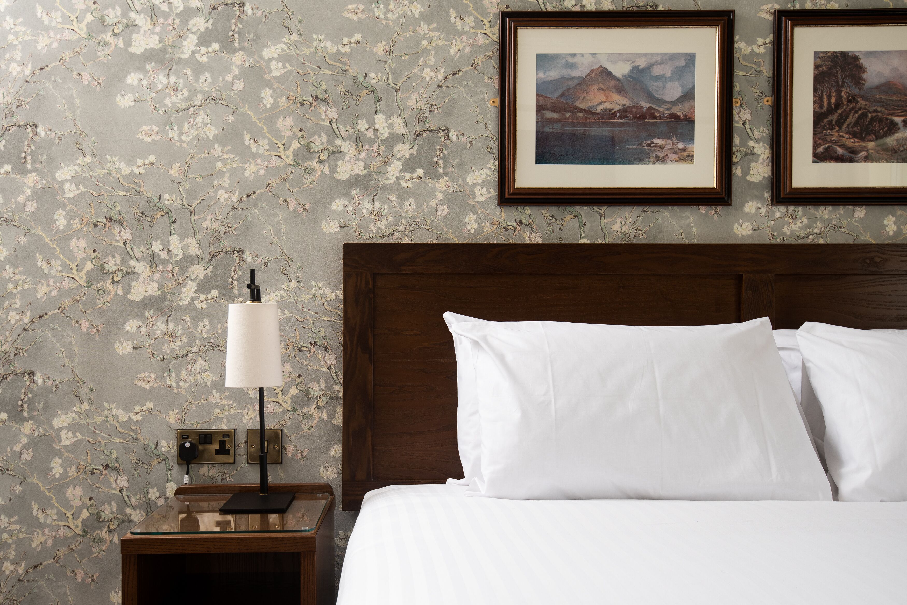 A neatly made bed with white linens, a wooden headboard, and a nightstand with a lamp.