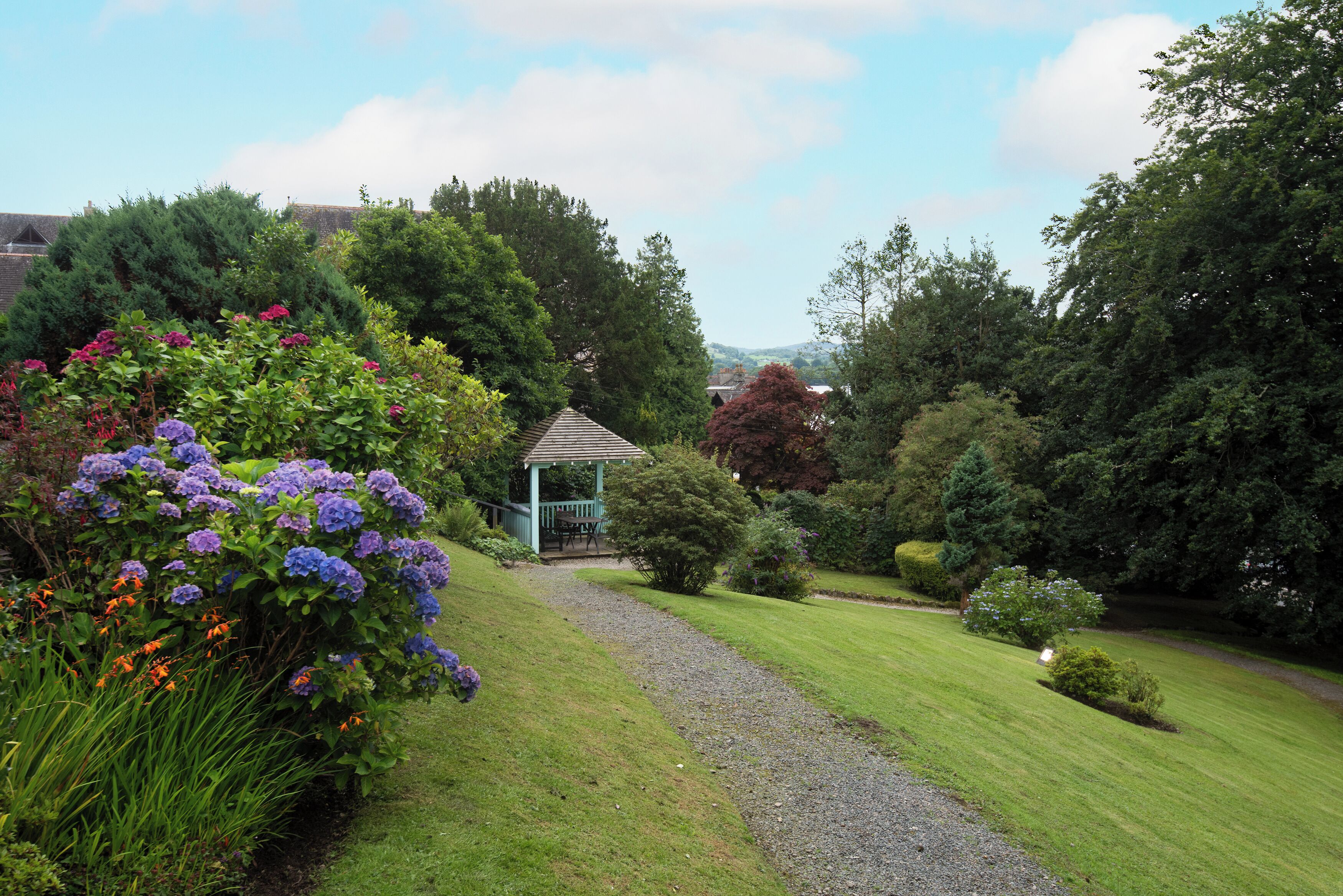 Ein Garten mit Laube, Kiesweg und verschiedenen Sträuchern und Blumen.