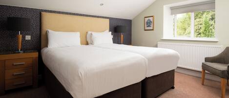 Ett hotellrum med två sängar, ett fönster med utsikt över träd, ett element och en stol.