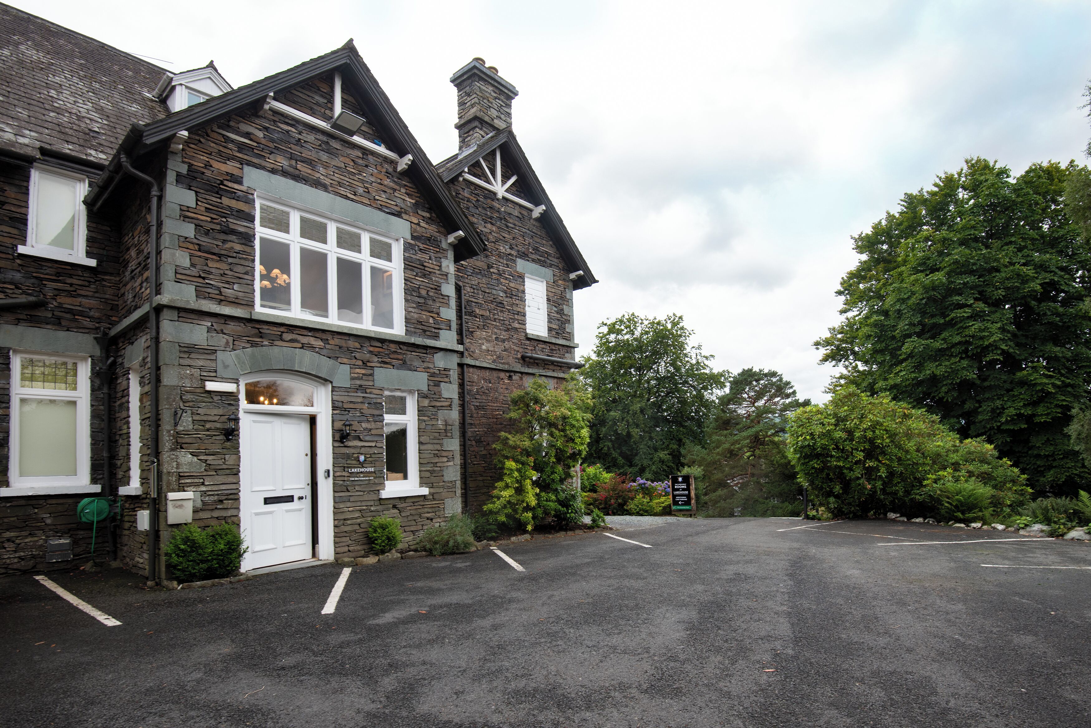 A stone building with a white door and windows, surrounded by greenery.