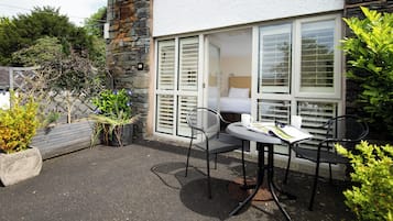A patio with a table and chairs, a bed visible through a window, and a stone wall.