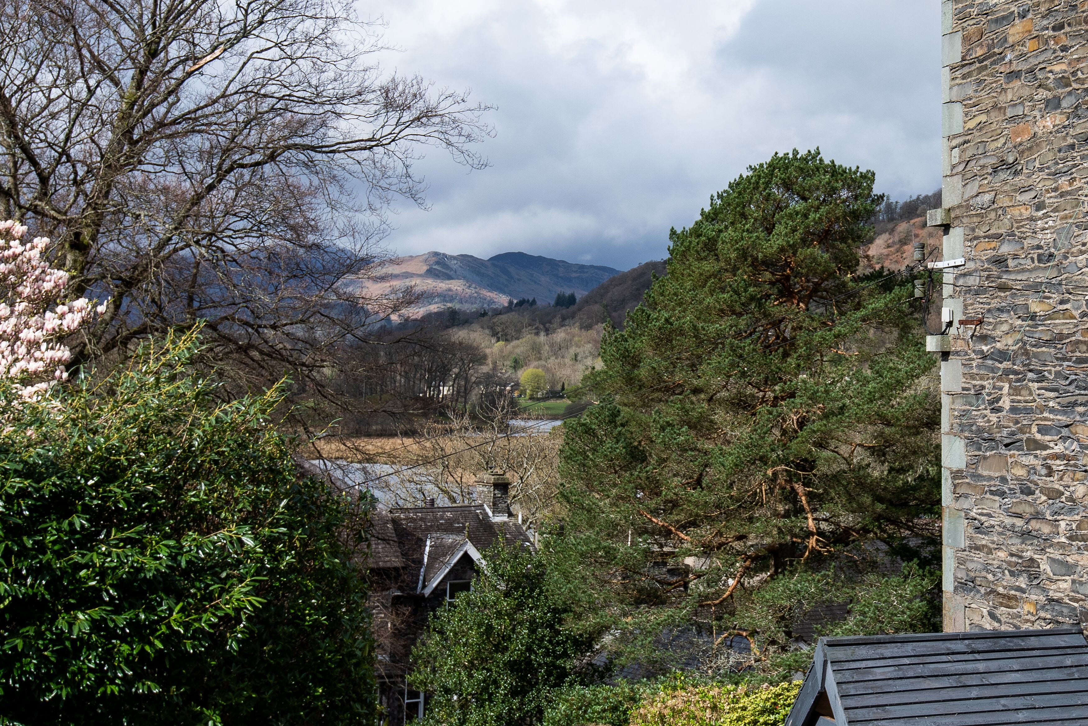 A stone building with a traditional roof, surrounded by lush greenery and a mountainous backdrop.