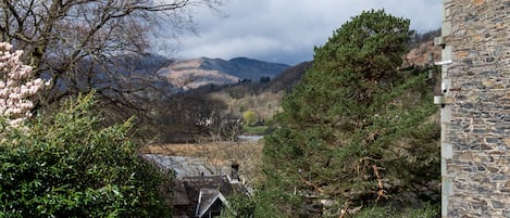 A stone building with a traditional roof, surrounded by lush greenery and a mountainous backdrop.