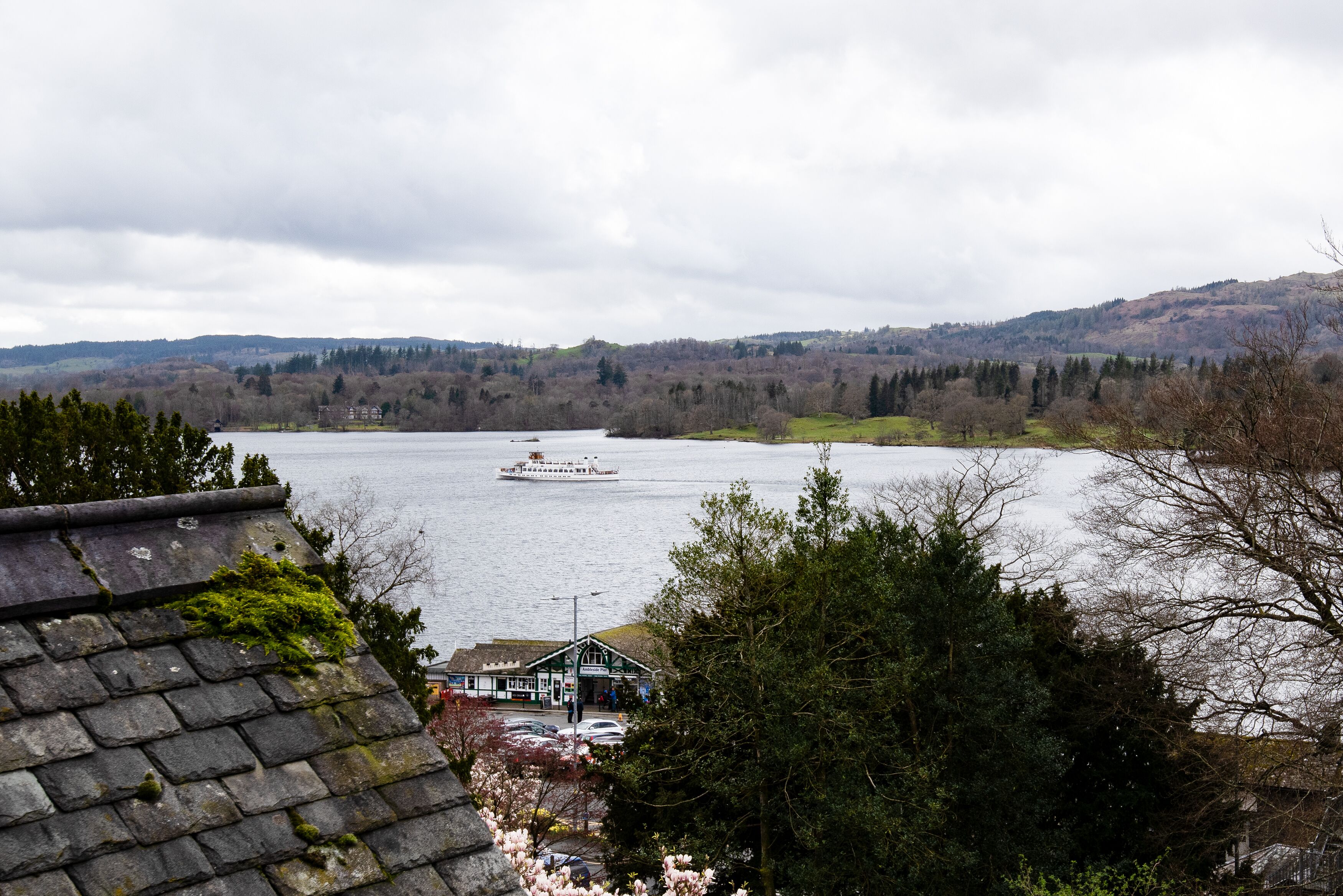 Blick auf einen Fluss mit einem Boot, einem Gebäude mit einem begrünten Dach und umliegenden Hügeln.