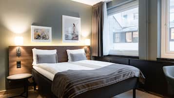 A modern hotel room with a large bed, two wall-mounted lights, a window with curtains, and a small round table.