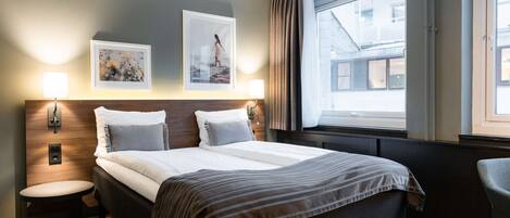 Habitación de hotel moderna con una cama grande, dos lámparas fijadas a la pared, una ventana con cortinas y una mesita redonda.