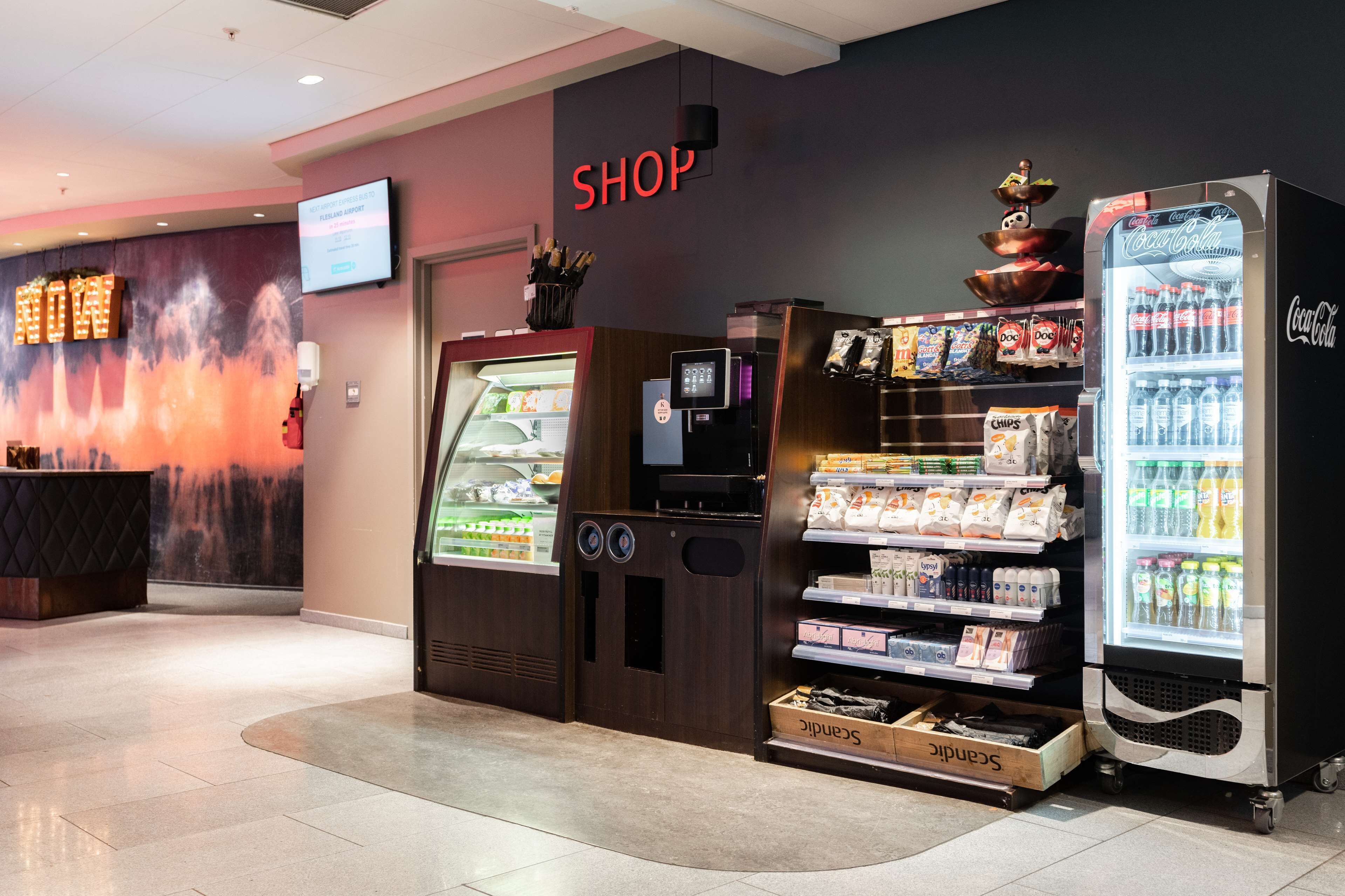 A shop area with a Coca-Cola refrigerator, a vending machine, and a display of snacks and beverages.
