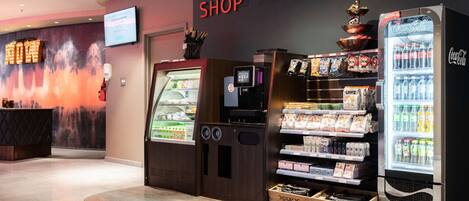 A shop area with a Coca-Cola refrigerator, a vending machine, and a display of snacks and beverages.