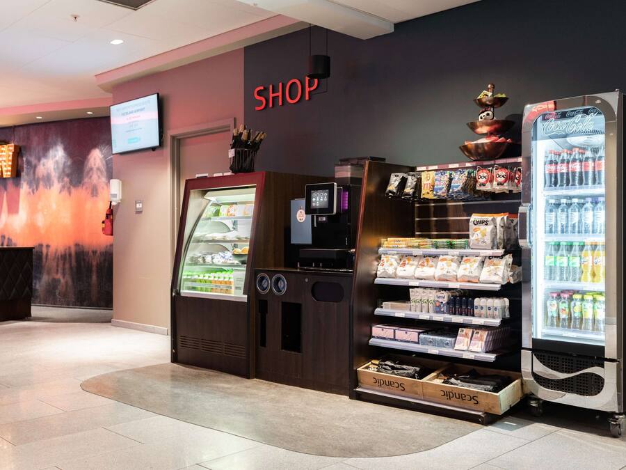 Un área comercial con un refrigerador Coca-Cola, una máquina expendedora y una exhibición de aperitivos y bebidas.
