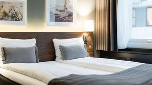 A hotel room with a neatly made bed, two framed pictures on the wall, a bedside lamp, and a window with curtains. - Scandic Bergen City (Bergen)