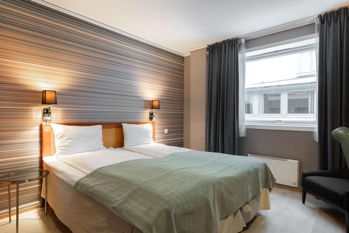 Een hotelkamer met een groot bed, twee bedlampen, een raam met gordijnen, een radiator en een stoel.