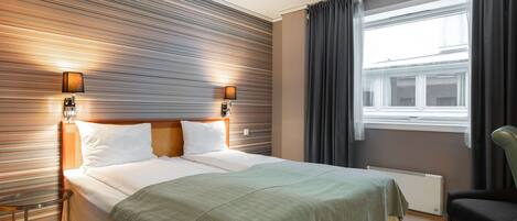 Habitación de hotel con una cama grande, dos lámparas de noche, una ventana con cortinas, un radiador y una silla.
