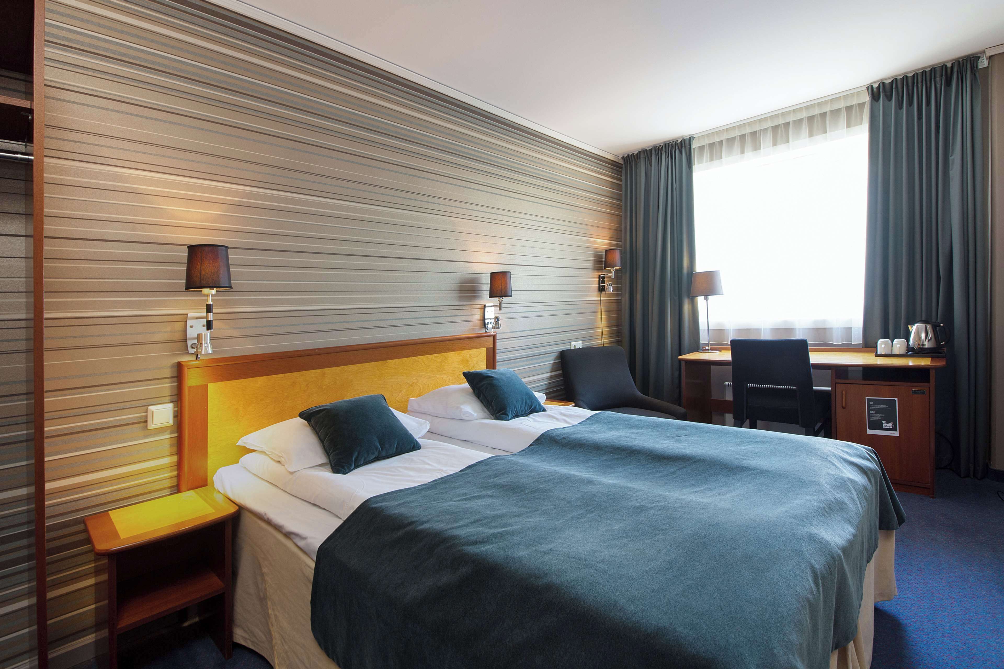 A hotel room with a large bed, bedside tables, a desk, and a chair.