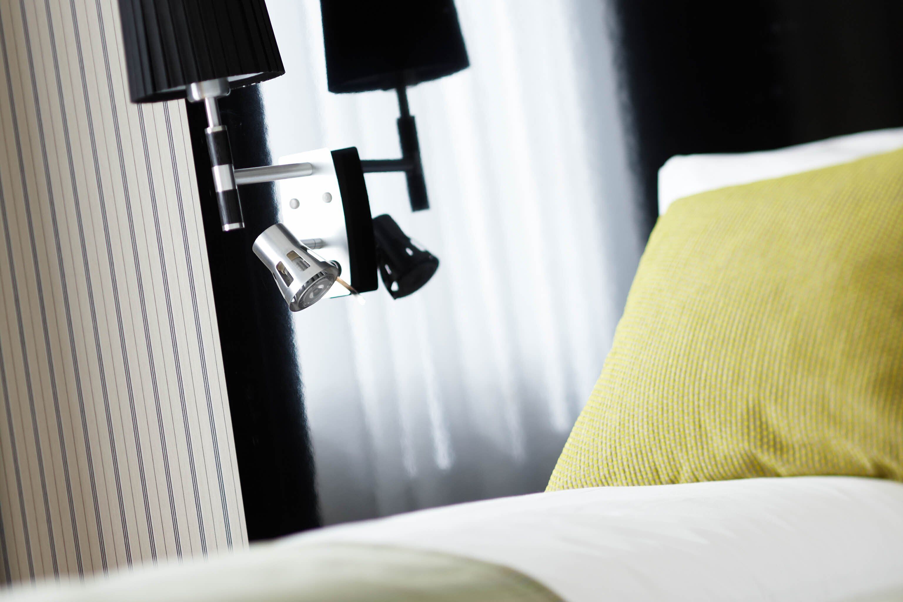 A hotel room with a bed, a nightstand, and a lamp.