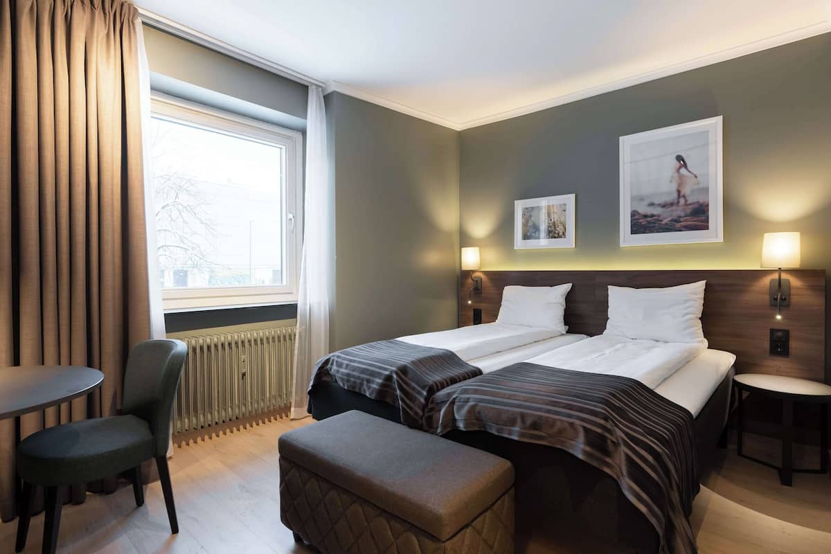 Een hotelkamer met twee bedden, een tafel, een stoel en een radiator.