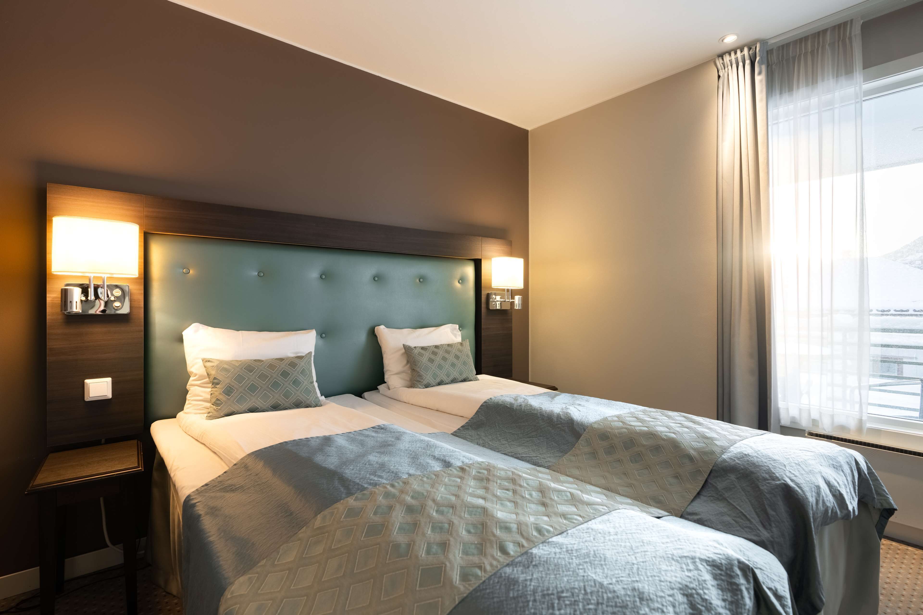 Ein Hotelzimmer mit einem großen Bett, zwei Nachttischen und einem Kopfteil mit integrierter Beleuchtung.