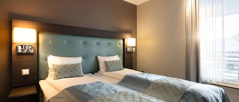 A hotel room with a large bed, two bedside tables, and a headboard with integrated lighting.