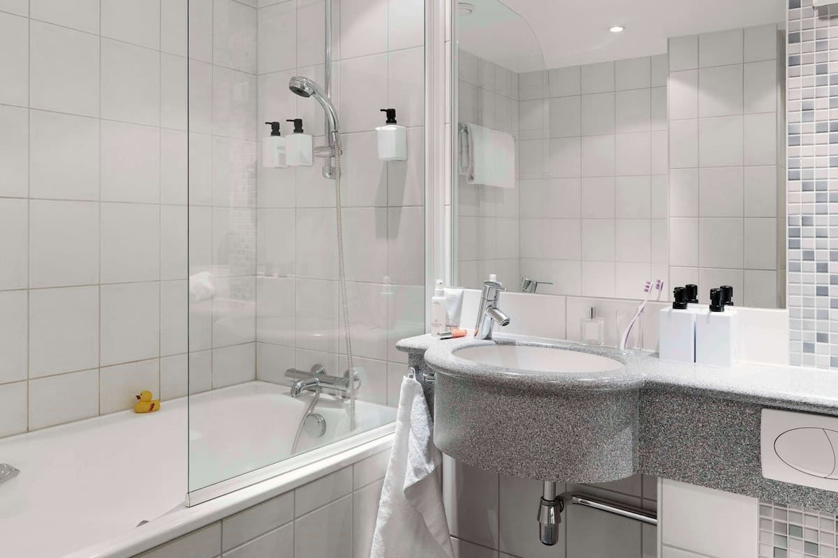 Een moderne badkamer met een douche met glazen wand, een granieten wastafel en een witte badkuip.