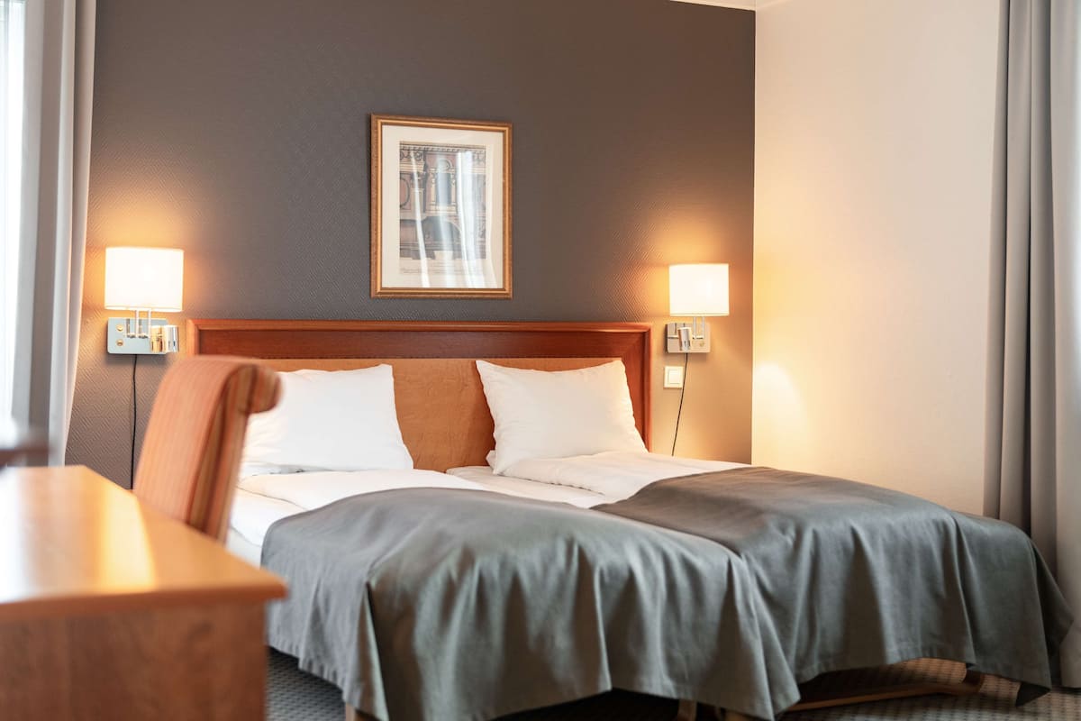 Een hotelkamer met een bed, twee bedlampen, een ingelijste foto aan de muur en een nachtkastje van hout.
